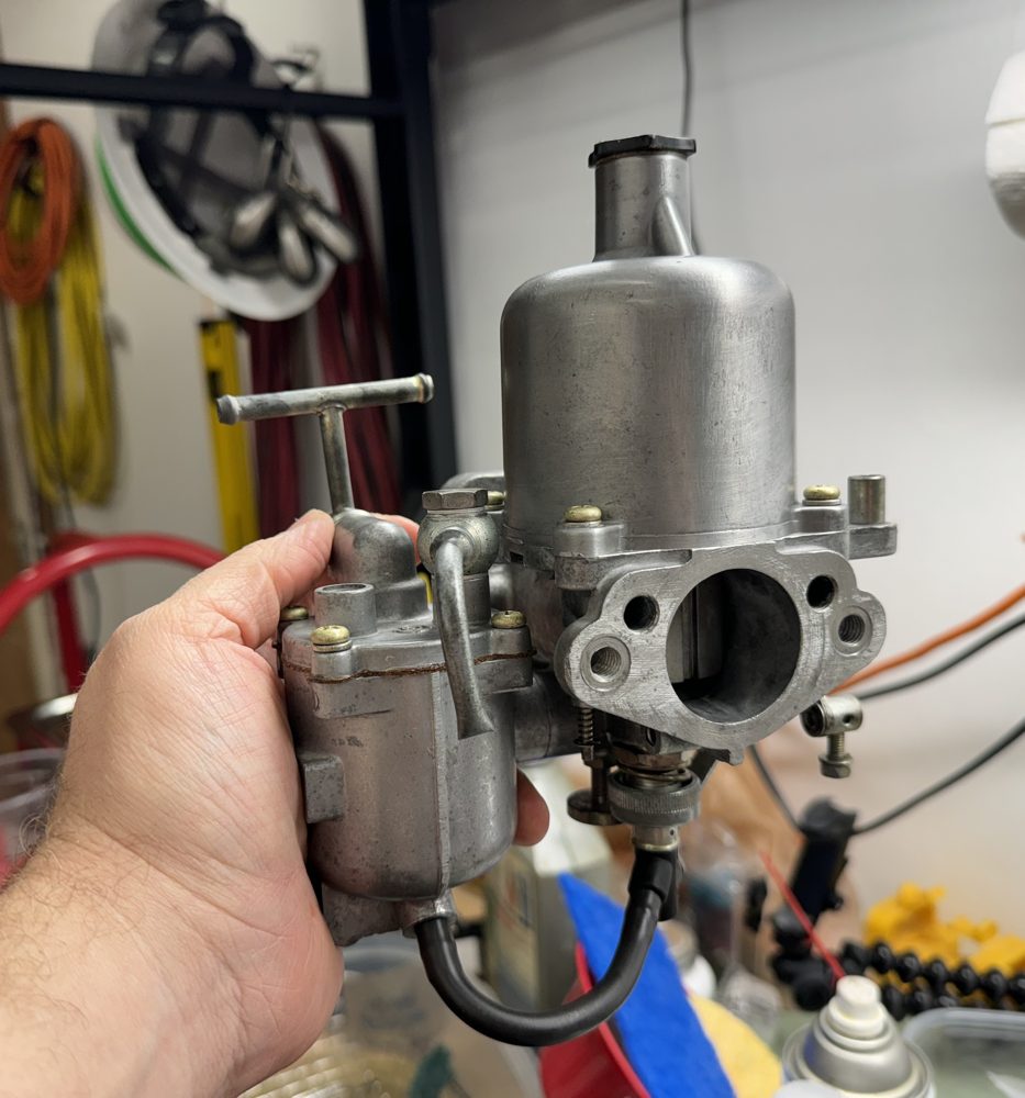 A hand holding a cleaned aluminum carburetor in a garage workshop