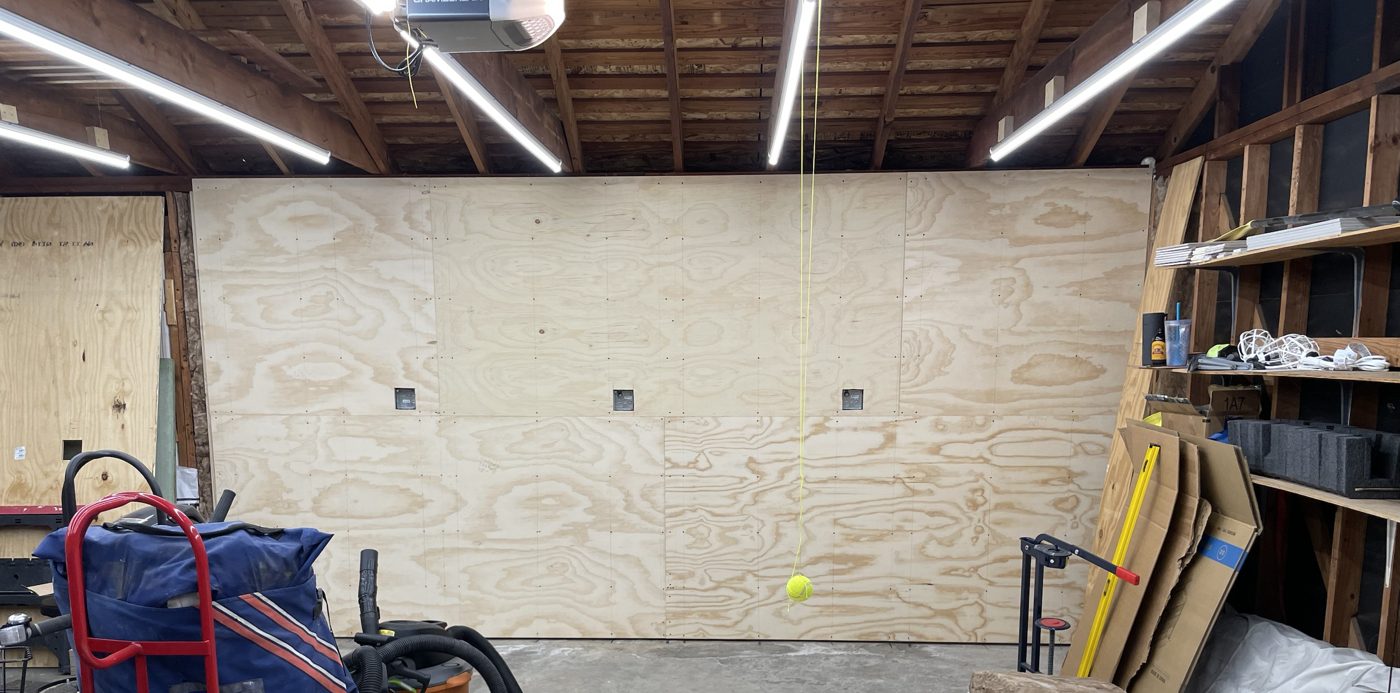 A garage wall freshly sheathed in plywood under rows of LED shop lights