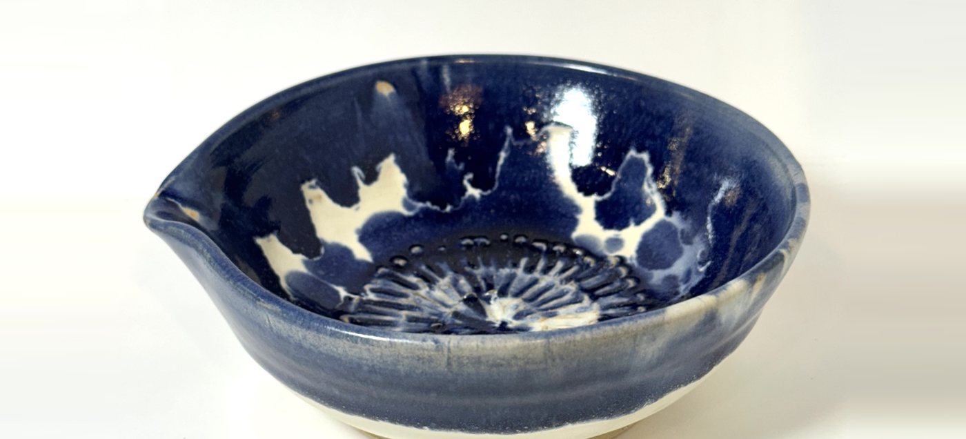Blue and white glazed bowl with a pour spout and a ridged grating surface in the base