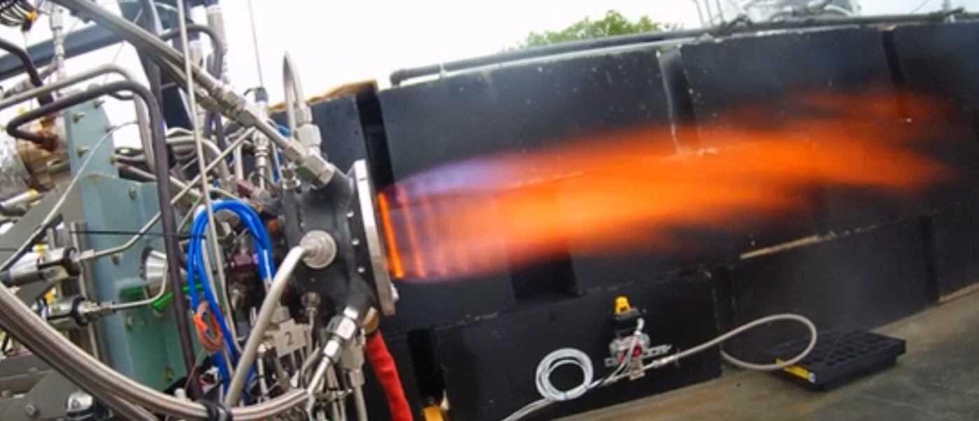 A rocket engine firing on a test stand with an orange exhaust plume