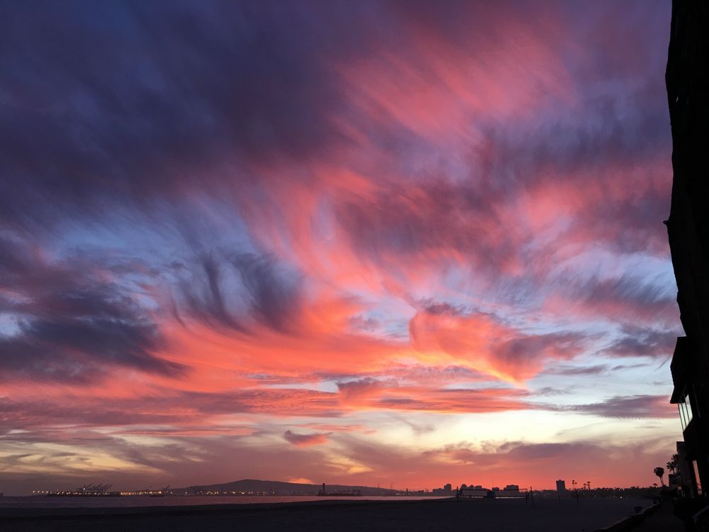 Pink and purple sunset clouds over a beach with port lights on the horizon